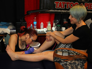 Artist Sid Avis tattoos on Sheri Mauer's foot Saturday afternoon. Jillian Danielson/RiverScene 