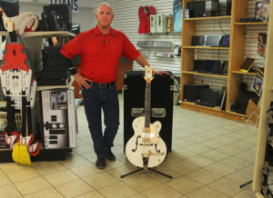 John Borders stand next to one of the items for sale in his shop, a Greutch Guitar. Jillian Danielson/RiverScene 