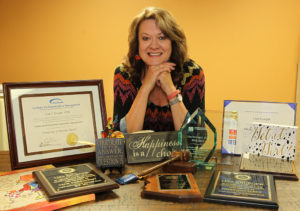 Lisa poses with things from around her office that makeup up some of who she is including awards, her love for chocolate, and even a Transformer that her grandkids play with. Jillian Danielson/RiverScene 